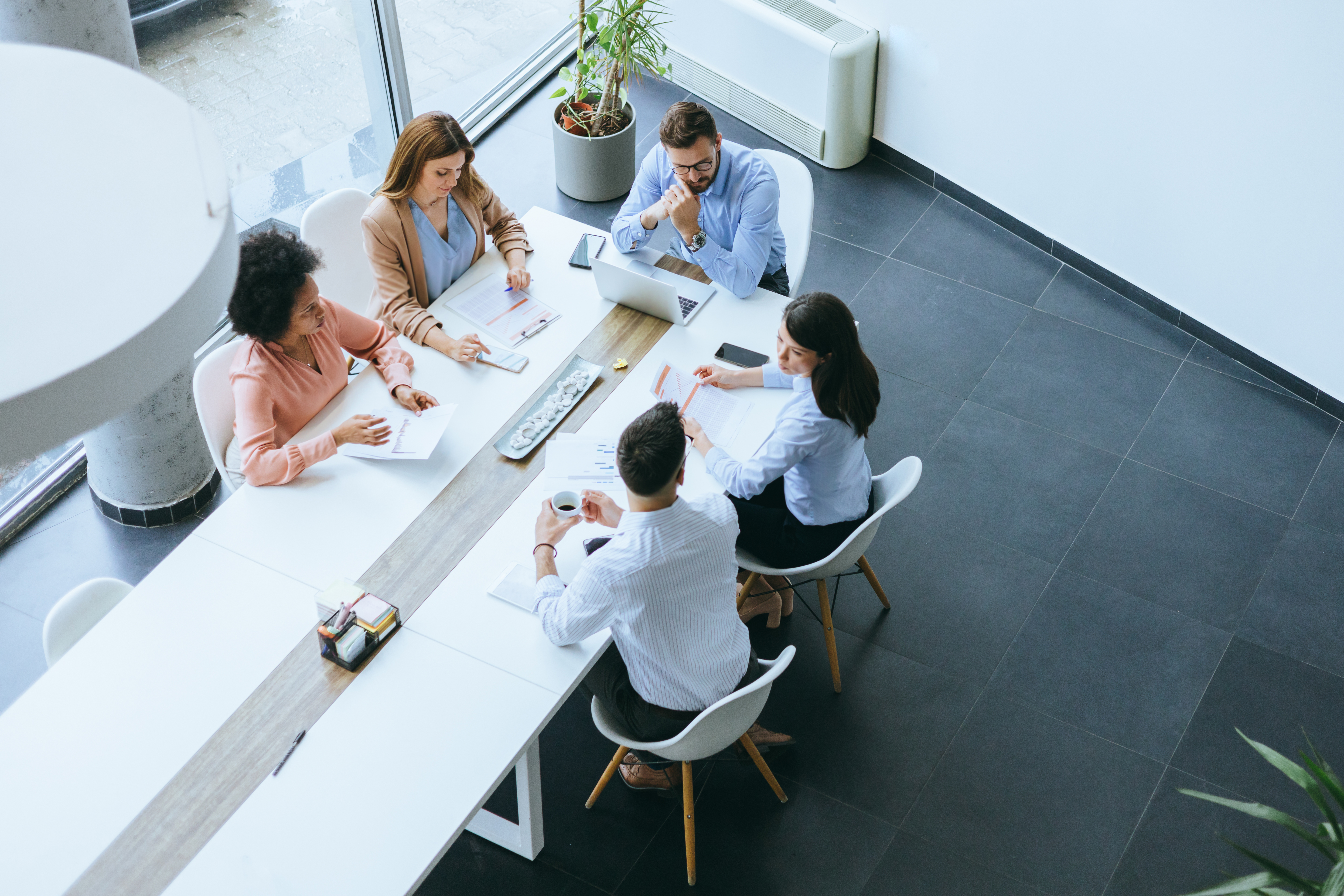 An overhead view shows a business team engaged in discussion around a lunch table, combining professional collaboration with a casual dining setting—reflecting networking, relationship building, and team culture.